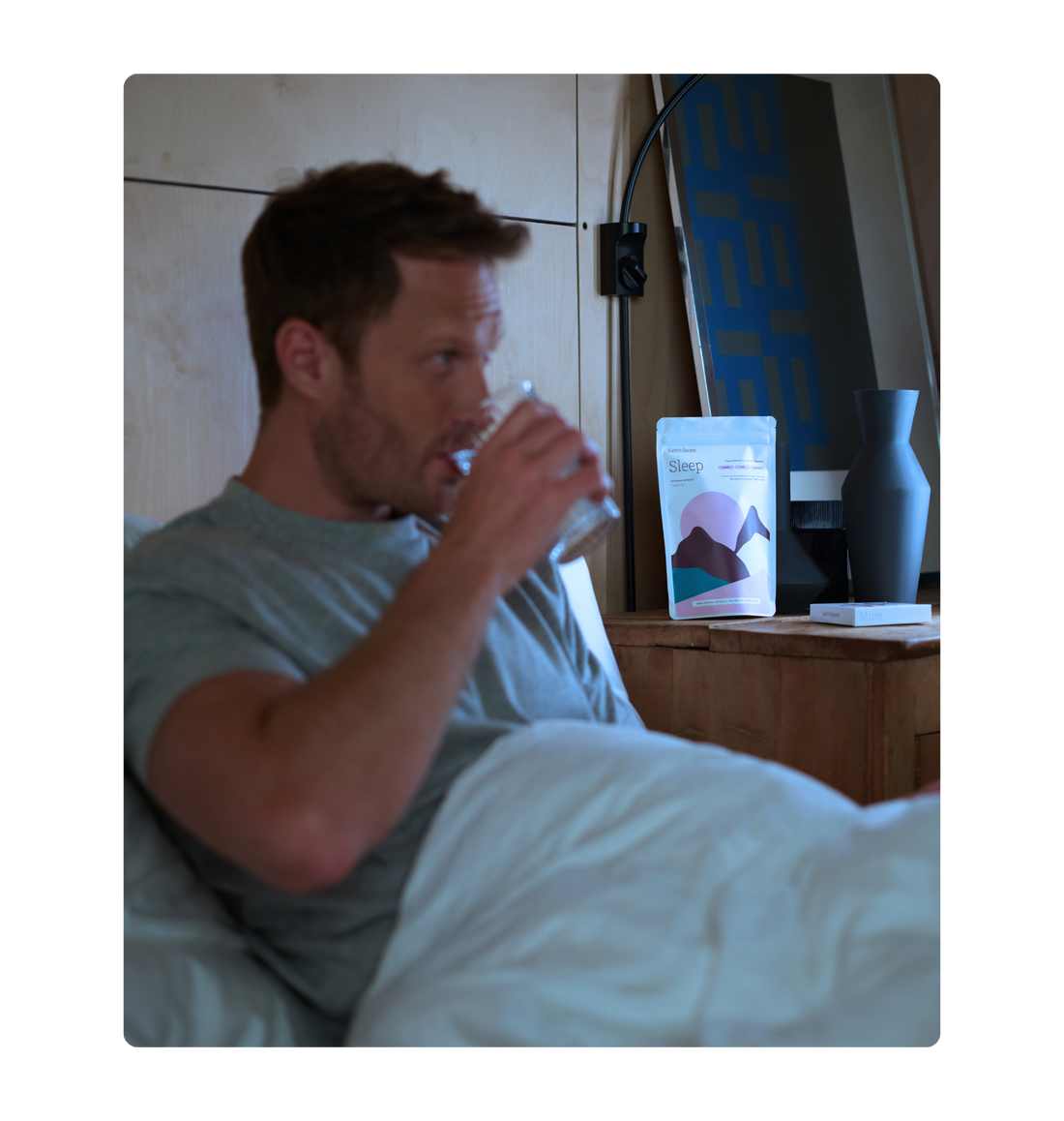 Man sitting up in bed at night, wide awake, drinking a glass of water