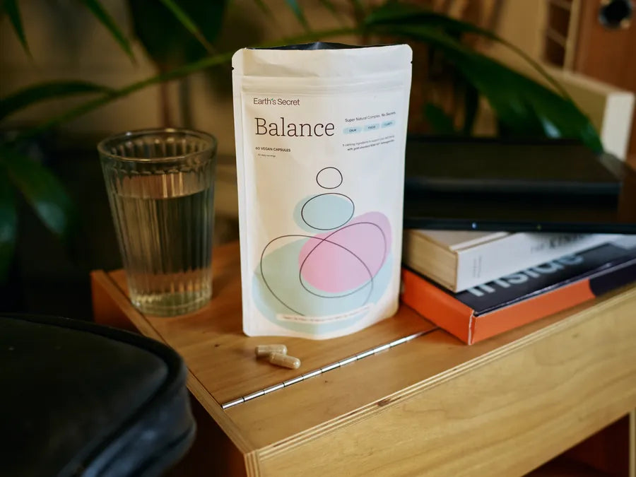 Earth&rsquo;s Secret Balance pouch with two capsules and a glass of water
