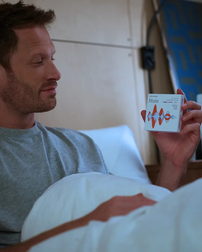 Man in bed holding a box of Mute ear plugs